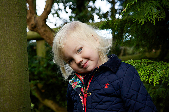 An outdoor children's portrait.  Little girl tilts head to look at the camera.