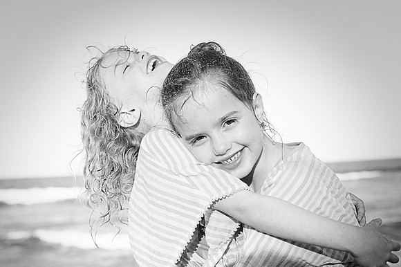 Sisters hug and laugh on a beach with sand filled hair.