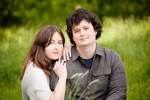 A young couple sat in long grass gazing towards the camera