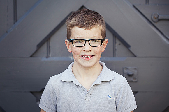 Young boy head and shoulders portrait, in front of grey door